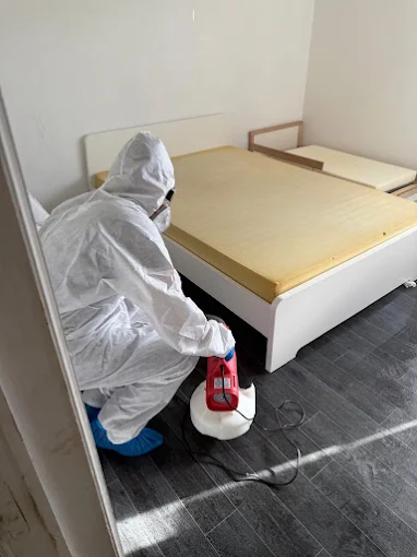 Technicien Deratihome accroupi au pied d’un lit, traitement contre les punaises de lit