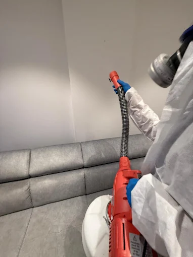 Technicien Deratihome appliquant un traitement le long d’un canapé